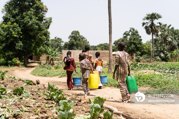 Group of black African children walking home with empty water containers after helping their father irrigate the family field