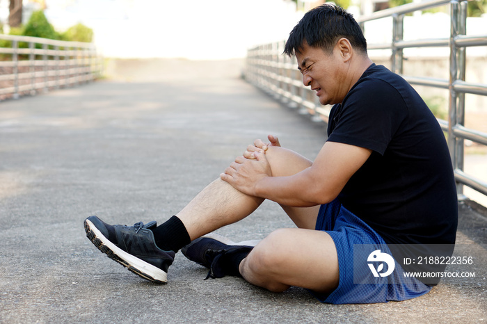 Asian Man runner gets hurt on his painful knee after running , jogging, exercise. Concept : injury knee twist sprain accident in workout or sport. Health problems. Copy space for text.