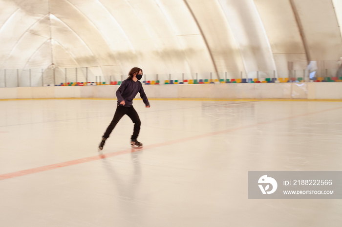 A masked man skates on ice. Indoor ice rink.