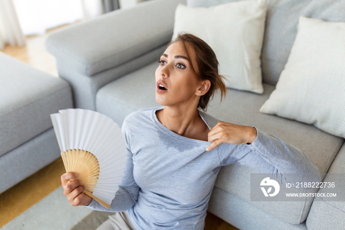 Stressed annoyed woman using waving fan suffer from overheating, summer heat health hormone problem, woman sweat feel uncomfortable hot in summer weather problem without air conditioner