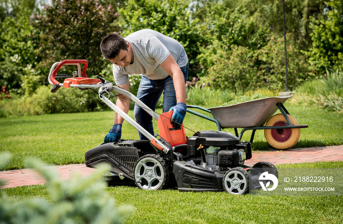 Gardener emptying lawn mower grass into a wheelbarrow after mowing.