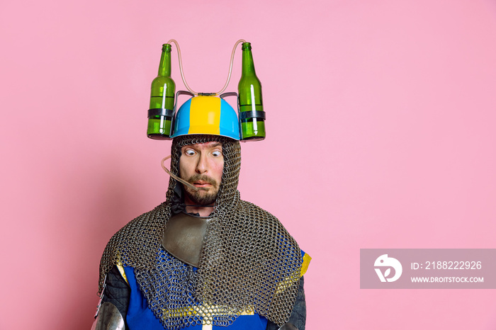 Half-length portrait of funny looking man, medieval warrior or knight in beer helmet and protective armor isolated over pink studio background