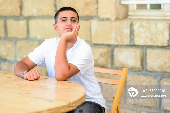 Black hair teenage boy sitting in high school yard at the table. Male student in college outdoor classroom.