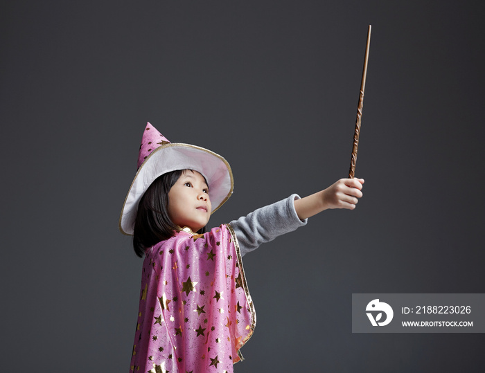 Cute Asian little girl wearing magic dress , playing with magic wand indoors