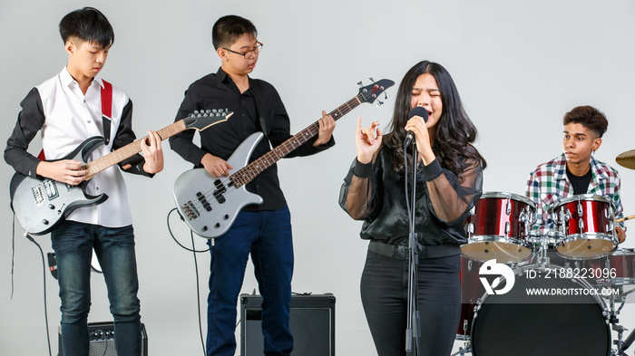 Group shot of teenage musicians playing the music and singing a song. Young students play bass guitar, electric guitar, drum, and keyboard. Concept of a school music band and teenager lifestyle