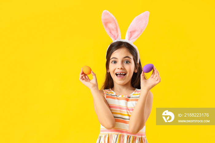 Happy little girl with bunny ears and Easter eggs on yellow background