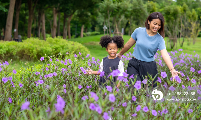 Happy mixed race family mother with little daughter holding hands and walking together in the garden. Smiling mom with cute child girl  enjoy and having fun in summer outdoor weekend holiday vacation