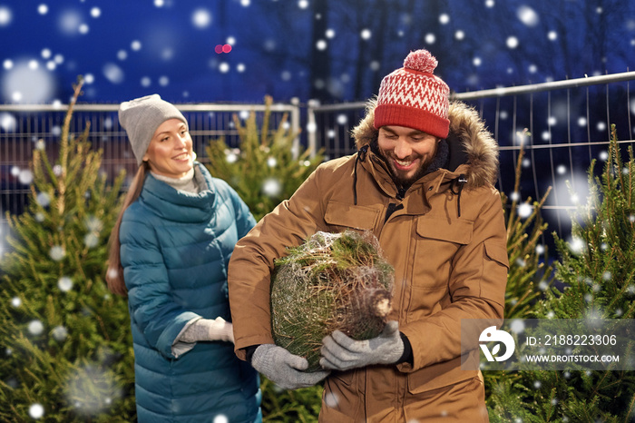 winter holidays and people concept - happy couple buying christmas tree at street market in evening over snow