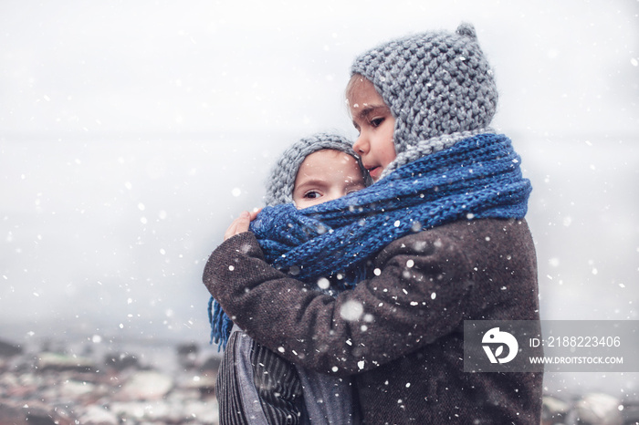 Girl in knitted grey hat hugging her frozen smaller brother