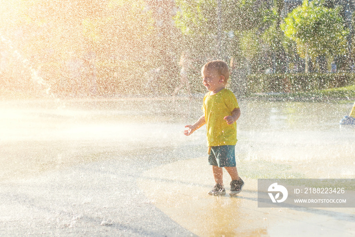 Happy child has fun playing in water fountains on hot day during summer. Boy playing in water at waterpark. A kid in spray park