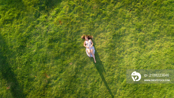 Aerial view. Young girl lying and resting on lawn on sunny day in park on grass. Above view. Woman on grass in meadow.