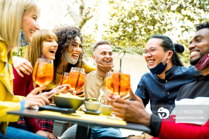 Multiracial friends wearing face masks drinking cocktails at bar restaurant - New normal friendship concept with young people enjoying meal in backyard party - Focus on guy in the middle