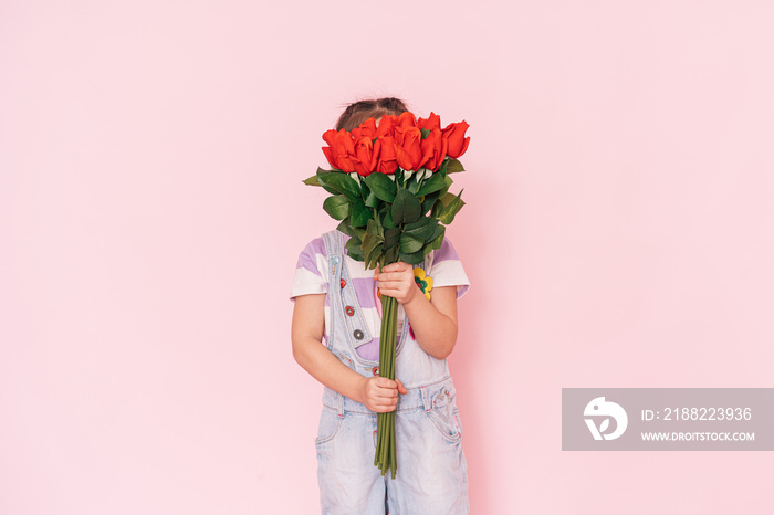 Little girl in overalls holding bouquet of roses against pink background. mother’s day