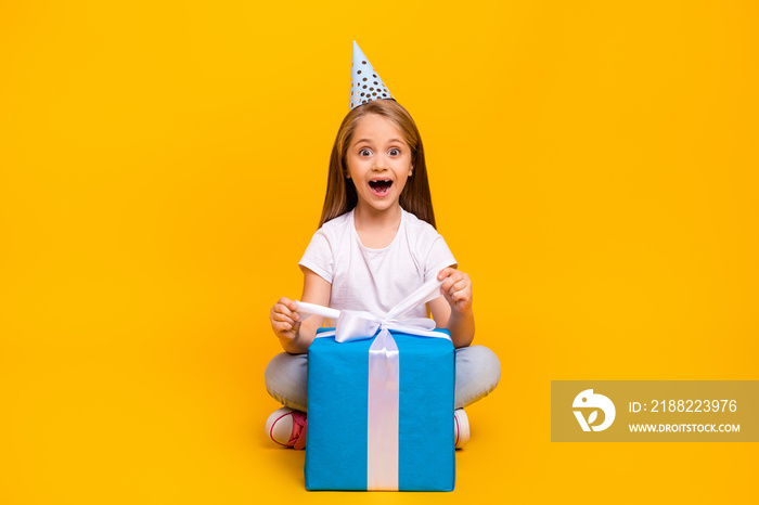 Full length photo of excited funky school girl wear white t-shirt birthday cap opening present isolated yellow color background