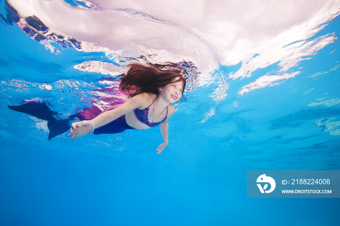 girl in a mermaid costume poses underwater in a pool.