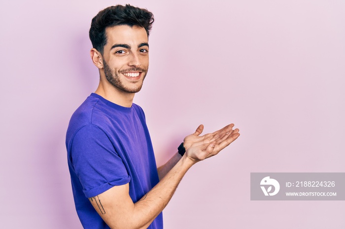 Young hispanic man wearing casual t shirt pointing aside with hands open palms showing copy space, presenting advertisement smiling excited happy