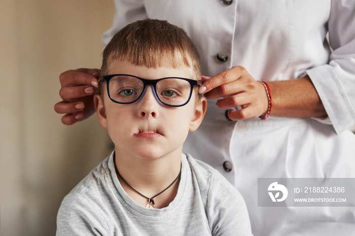 Child making faces to the camera. Kid sitting in the doctor office and trying new blue glasses