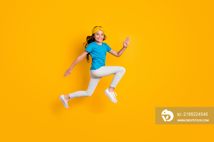 Full body profile photo of funny little lady jumping high good mood cheerful jogging competition race wear casual blue t-shirt headband trousers shoes isolated yellow color background