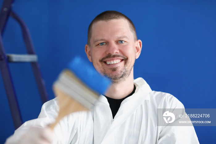 Smiling repairman holding construction brush with blue paint