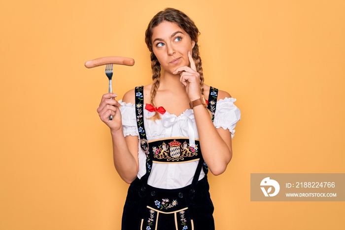 Beautiful german woman with blue eyes wearing oktoberfest dress holding fork with sausage serious face thinking about question, very confused idea