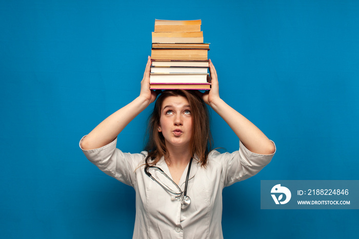 young beautiful funny girl the nurse holds many books on a blue background and is surprised, the student is studying in a medical college