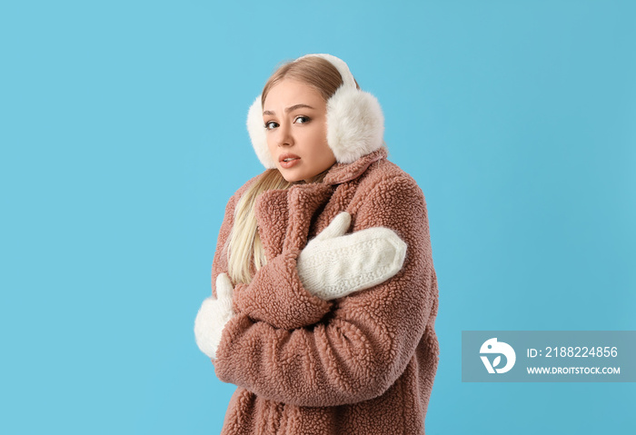 Frozen woman in winter clothes, mittens and fur earmuffs on blue background