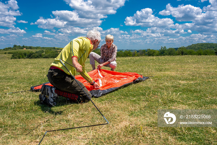 Senior couple having fun together while putting up a tent in nature with beautiful landscape in the background