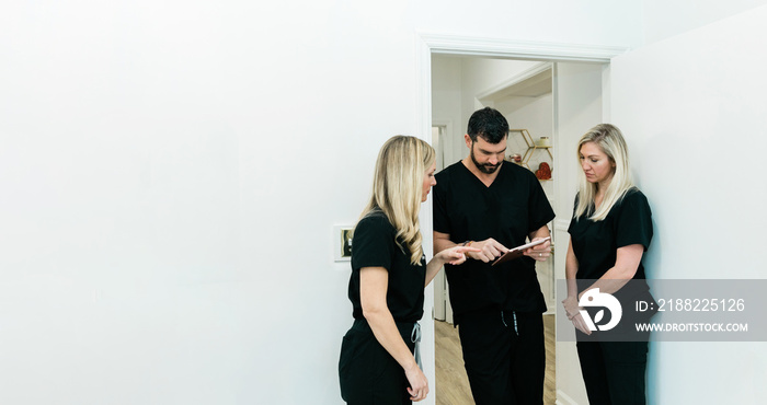 A male physician doctor at a medical spa and wellness clinic speaking to two female nurse practitioners