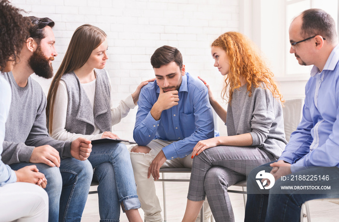 People comforting depressed addict man at rehab group meeting