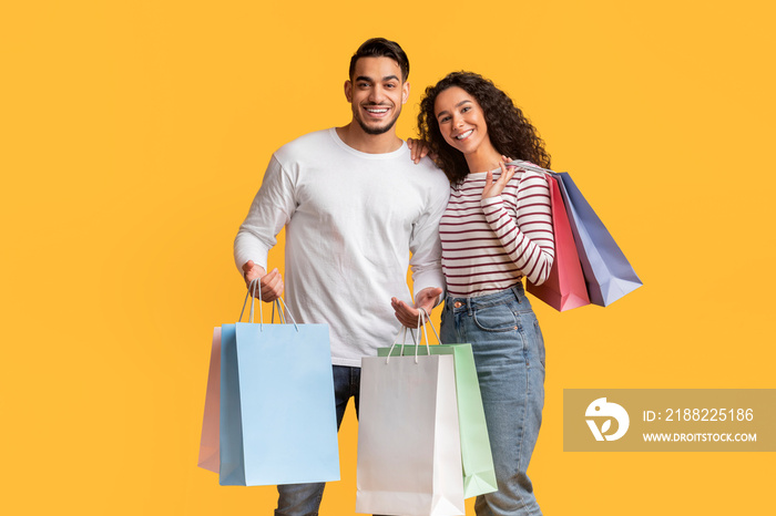 Middle Eastern Couple Posing With Shopping Bags In Hands Over Yellow Background