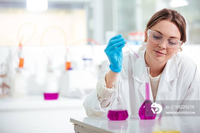 young woman scientist working with a pipette in a laboratoy glassware  with pink liquid in a lab