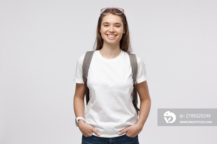 Smiling girl wearing white t-shirt and backpack, isolated on gray background