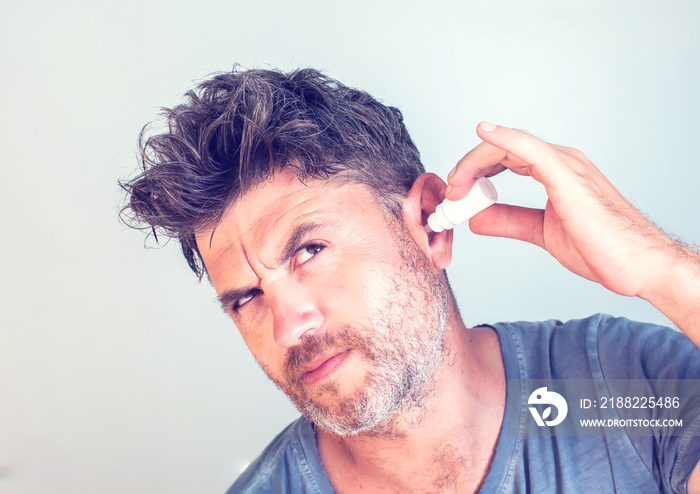 man using ear drops on gray background