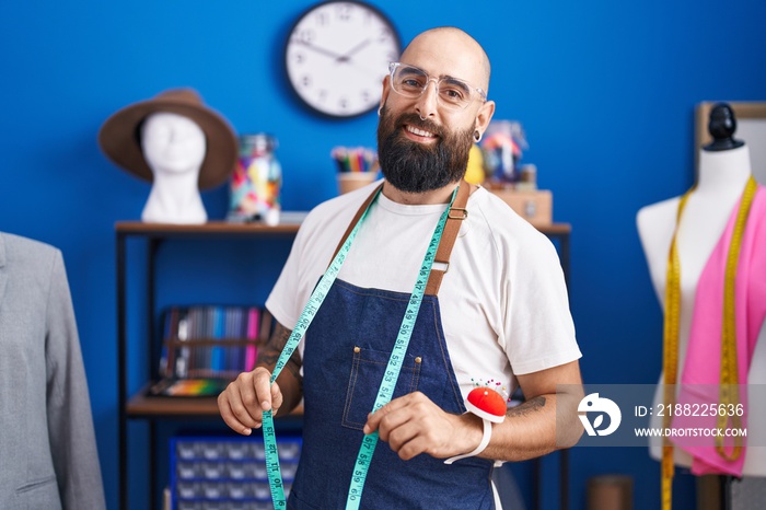 Young bald man tailor smiling confident standing at clothing factory