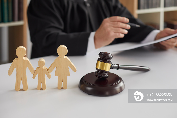 Close up of wooden figurines of family with child and gavel on background of judge conducting divorce process. Concept of alimony, family law and child custody.