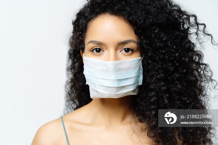 Serious Afro American woman tries to stop virus and epidemic disease, stays at home during infectious outbreak, wears medical mask, isolated on white background, being hospitalized, diagnosed