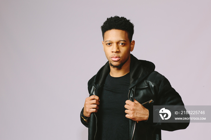 Portrait of a cool guy holding his jacket and looking at camera, isolated on grey studio background