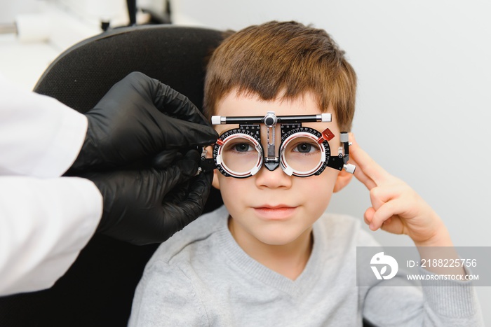 Small serious boy sitting on chair office of vision test. doctor picks up lenses to special glasses