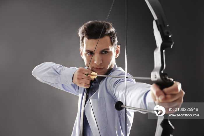 Young businessman practicing archery on dark background