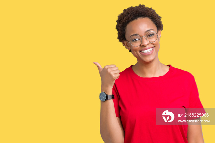 Beautiful young african american woman wearing glasses over isolated background smiling with happy face looking and pointing to the side with thumb up.