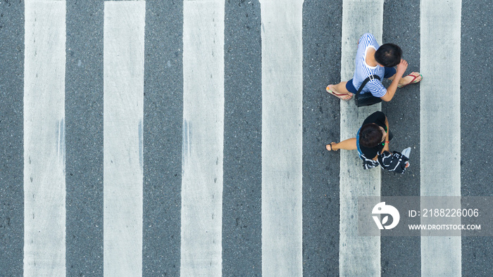 the top view of couple people walk across the pedestrian crosswalk in white and grey pattern