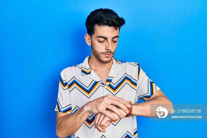 Young hispanic man wearing casual clothes checking the time on wrist watch, relaxed and confident