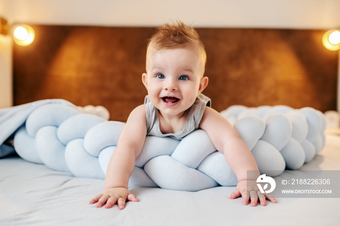 Adorable caucasian smiling baby boy lying on stomach on bed in bedroom and looking up. Baby have two teeth.