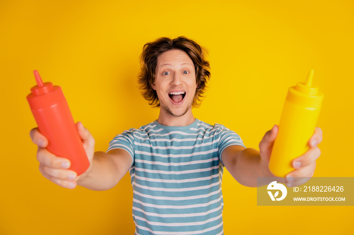 Closeup view of young guy holding bottle of ketchup mustard spices cook food isolated over yellow color background