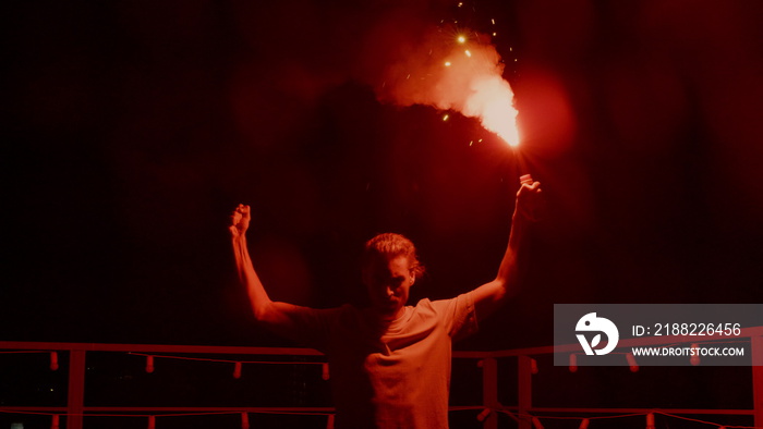 Aggressive man burning signal flare on roof. Football fan standing with fire