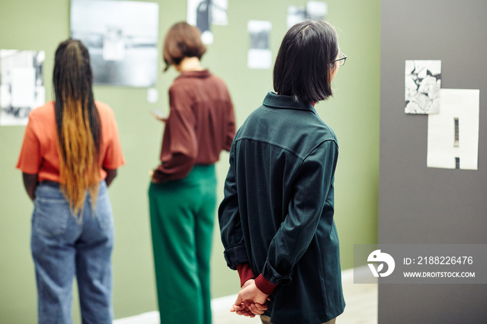 Unrecognizable young people looking at black and white photos on walls at modern photography exhibition in university