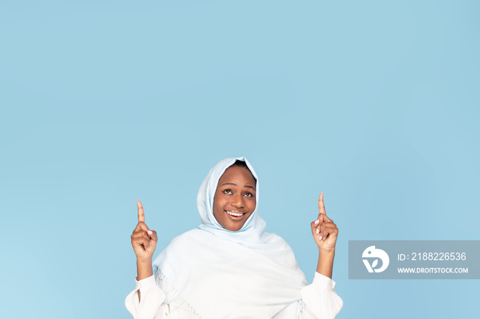 Check this. Happy black woman in hijab pointing up at copy space above her head, demonstrating free place for your ad