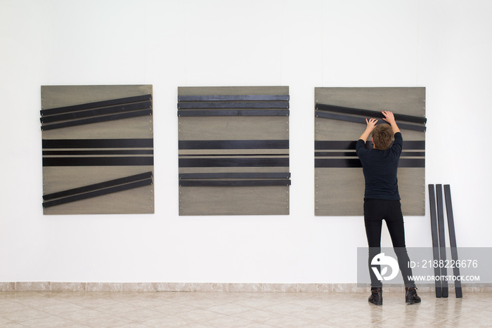 Woman artist assembling modern art installation on the art gallery wall