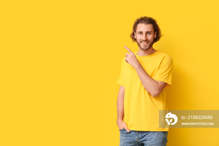 Handsome young man in stylish t-shirt pointing at something on yellow background