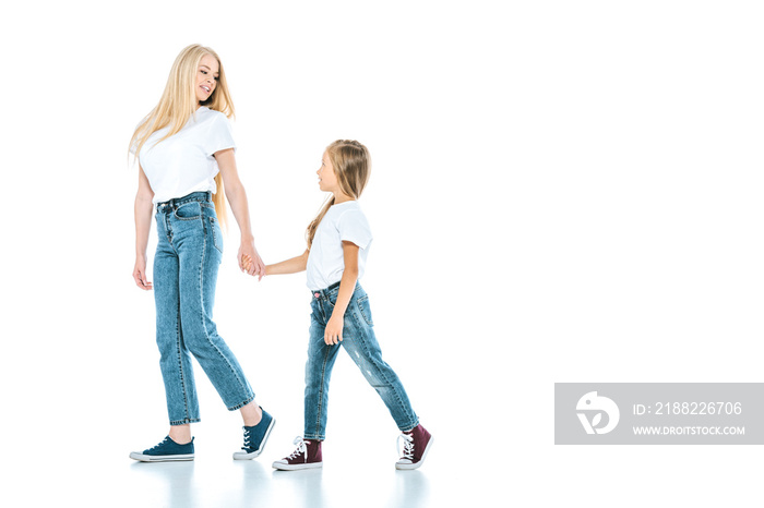 happy mother holding hands with kid and walking on white